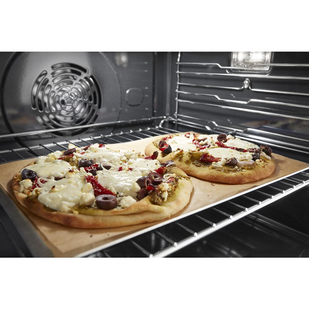 Two homemade pizzas baking on a rack inside a stainless steel single wall oven with true convection.