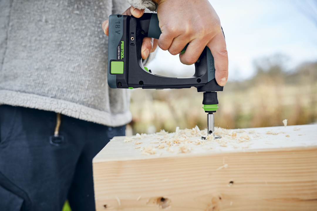 Person using Festool cordless drill to bore a hole into thick wooden plank outdoors for home improvement project