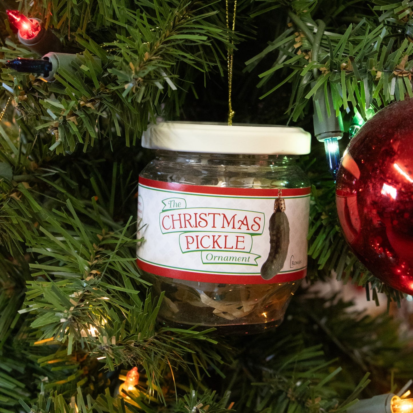 Clear glass jar with white lid hanging on Christmas tree holding a green pickle ornament in holiday decor collection