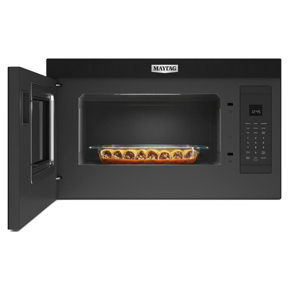 Black over-the-range built-in microwave with door open showing glass dish of cooked food inside in kitchen appliances collection