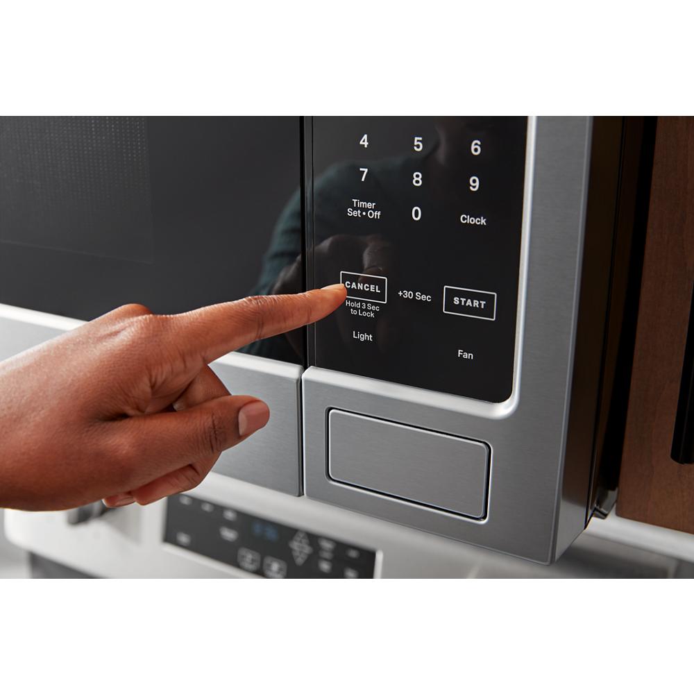 Finger pressing cancel button on stainless steel over-the-range microwave control panel in kitchen setting