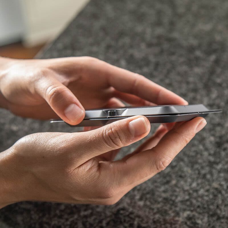 Person holding a sleek smartphone above a dark granite countertop in a casual home setting