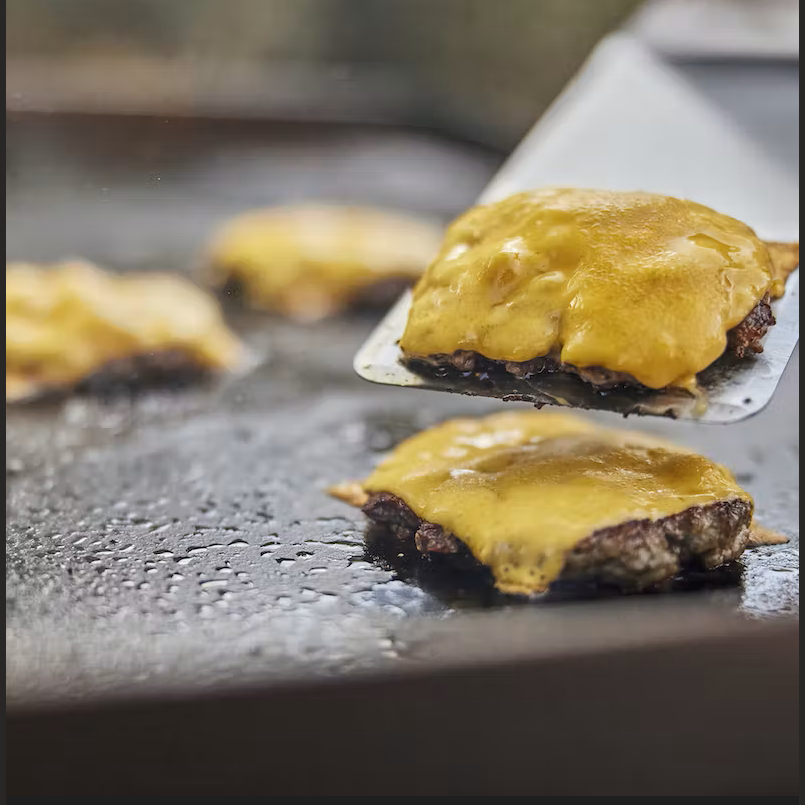Flat top griddle spatula lifting cheeseburger patty on stainless steel cooking surface for tools and home use