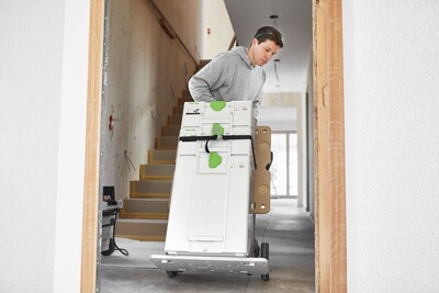 Man moving a Festool tool on a hand cart through a hallway in a home improvement setting