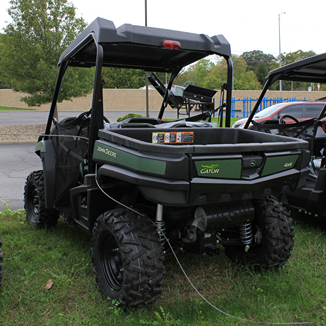 Green John Deere utility vehicle with Maxxis Bighorn tires parked on grass at outdoor equipment display
