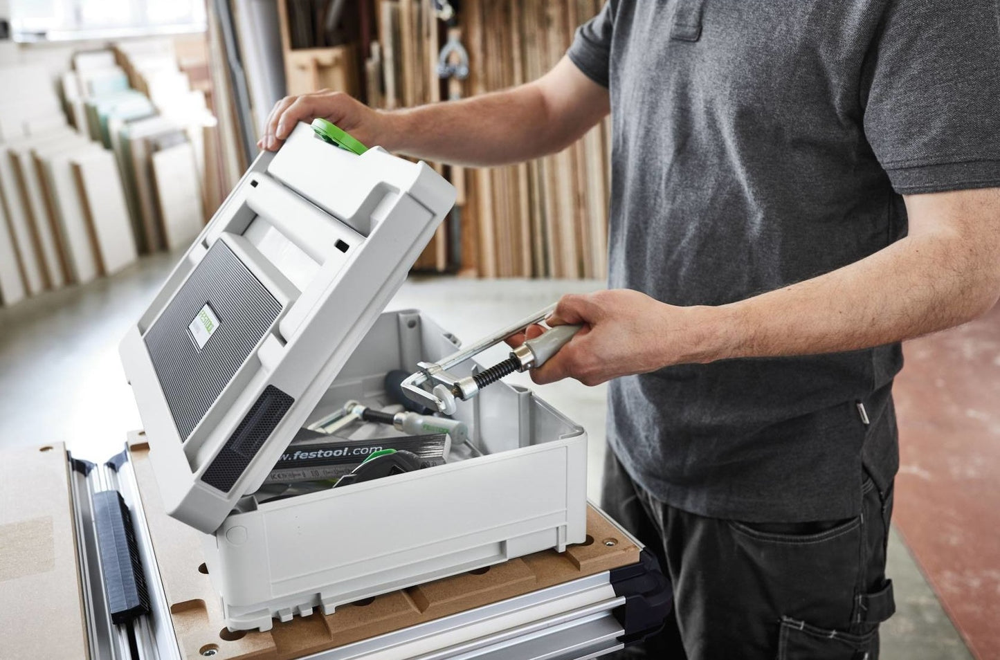 Person opening a compact white toolbox with tools inside on a woodworking workspace