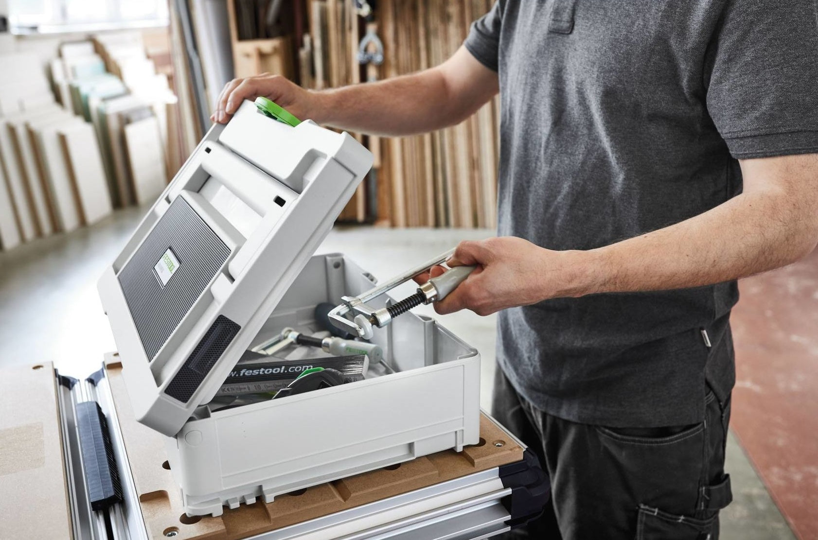 Person opening a compact white toolbox with tools inside on a woodworking workspace