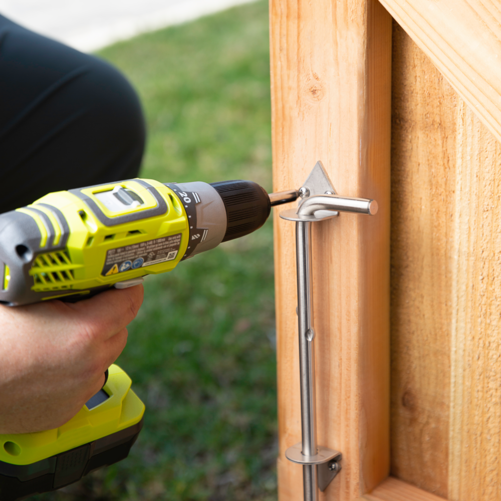 Person using cordless drill to install stainless steel cane bolt on wooden gate in door and gate accessories under $50
