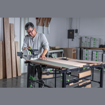 Man using Festool cordless track saw with kickback stop on large workbench in workshop for home improvement tools