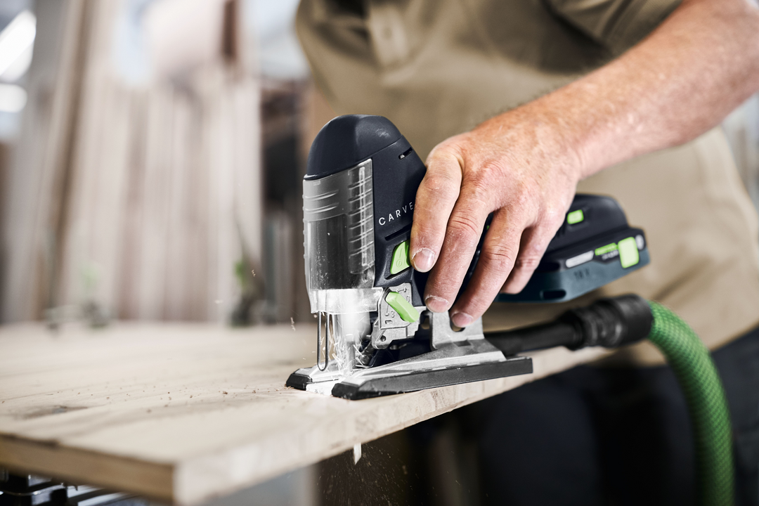 Cordless barrel grip jigsaw cutting wood with dust extraction in a home improvement workshop setting
