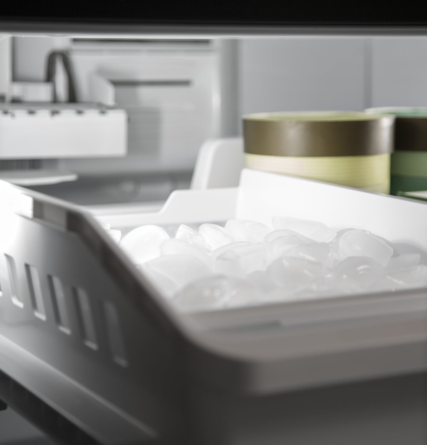 Open freezer drawer with clear ice cubes and containers inside a bottom-freezer refrigerator from appliances collection