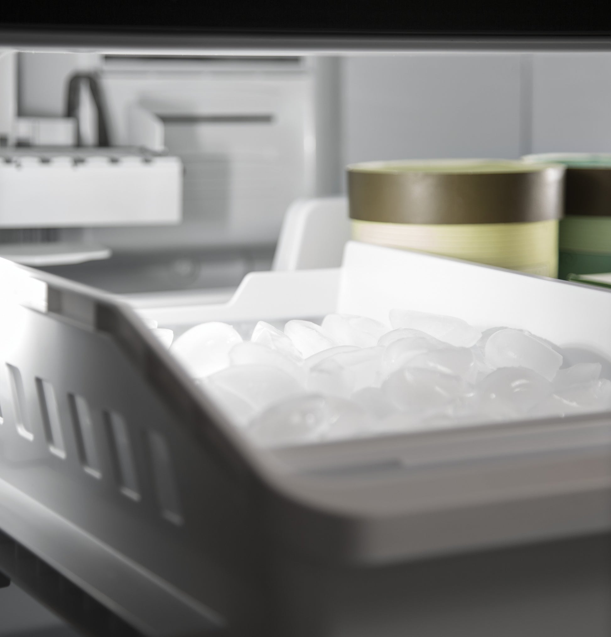 Open freezer drawer with clear ice cubes and containers inside a bottom-freezer refrigerator from appliances collection