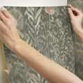 Hands smoothing taupe peel and stick wallpaper with subtle floral dandelion design for easy home improvement tasks