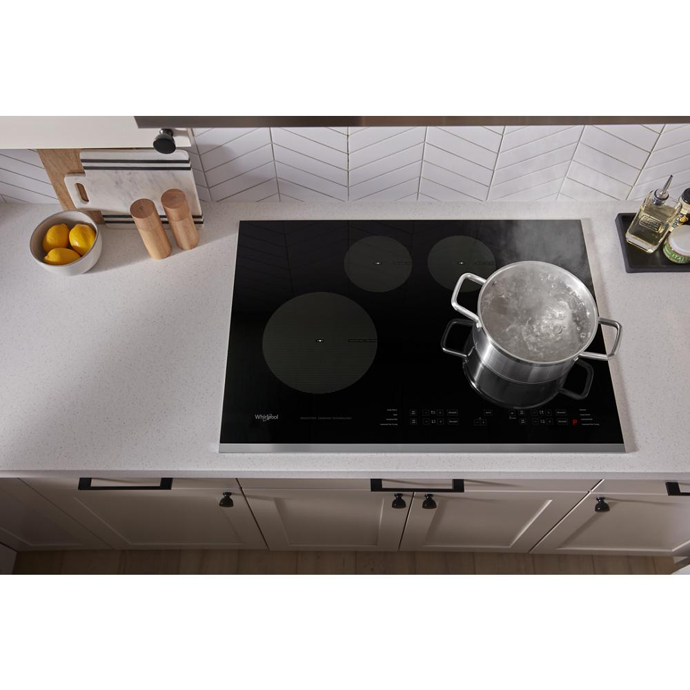 Black glass 30-inch induction cooktop with boiling pot on modern white kitchen countertop and utensils nearby