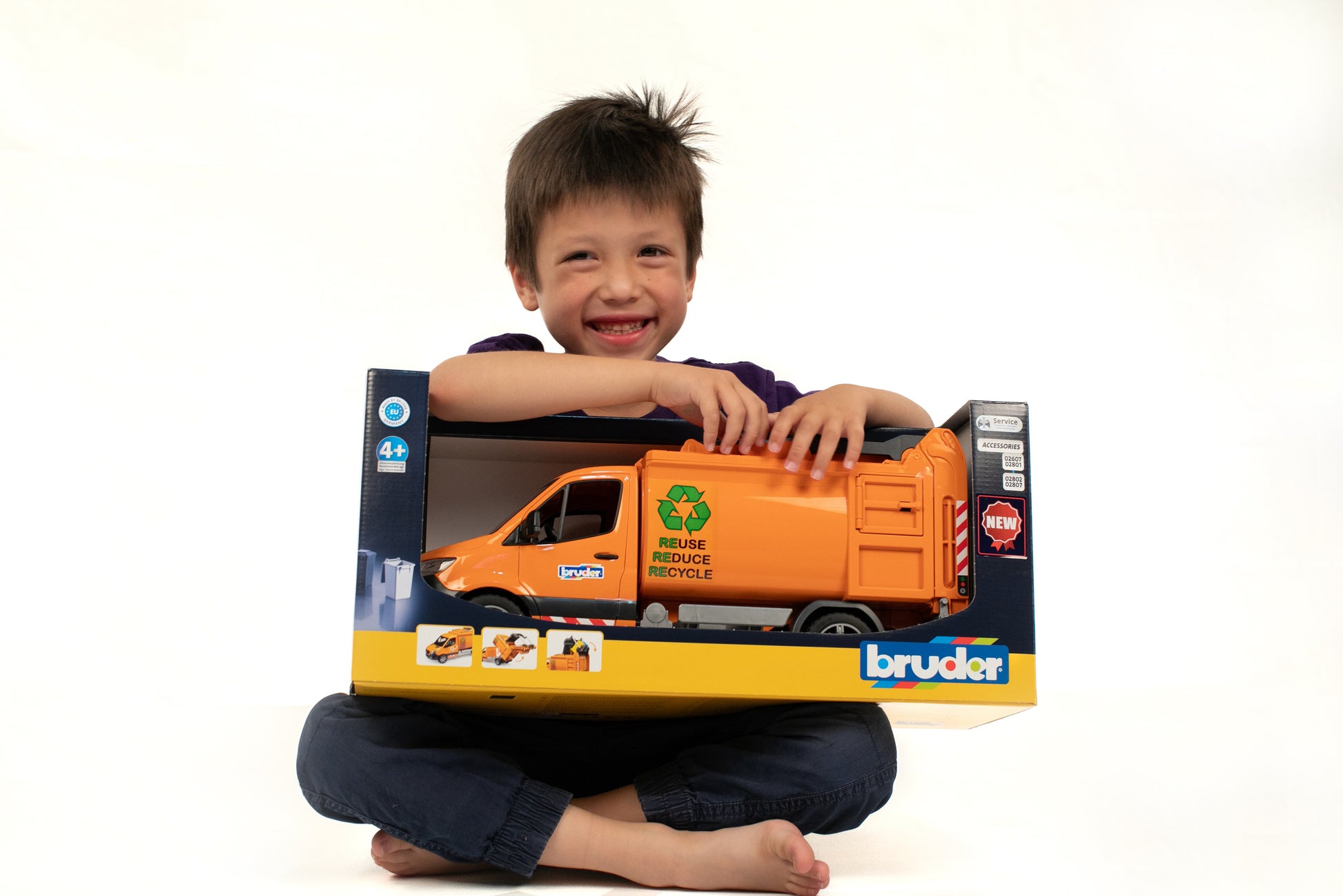 Child smiling while holding Bruder orange MB Sprinter garbage service toy truck in boxed packaging for home improvement play