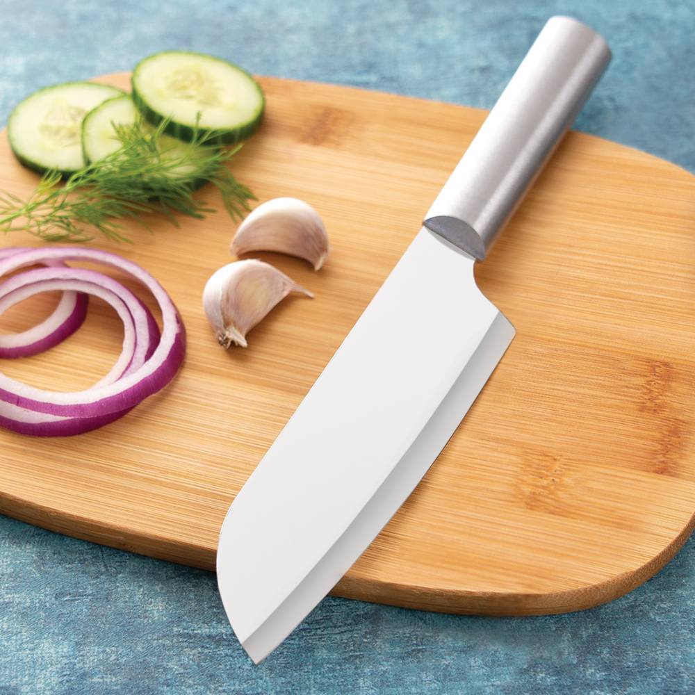Stainless steel cooks knife with smooth metal handle resting on wooden board with sliced vegetables and garlic cloves