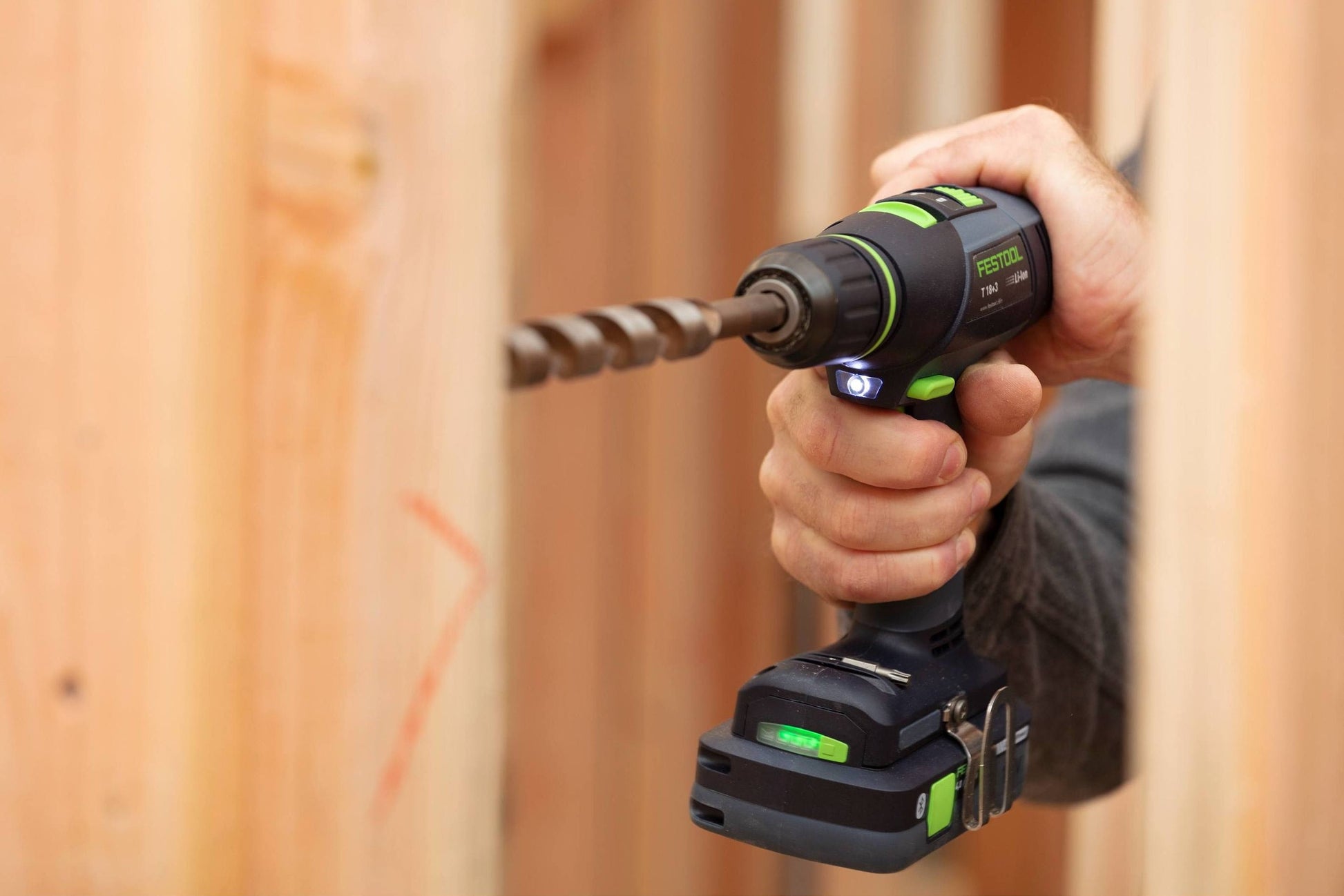 Handheld Festool cordless impact driver drilling into wood with LED light on and battery powered tool in use