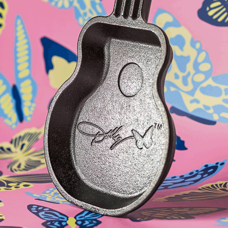Mini cast iron skillet shaped like a guitar with Dolly Parton signature on a colorful butterfly-patterned background