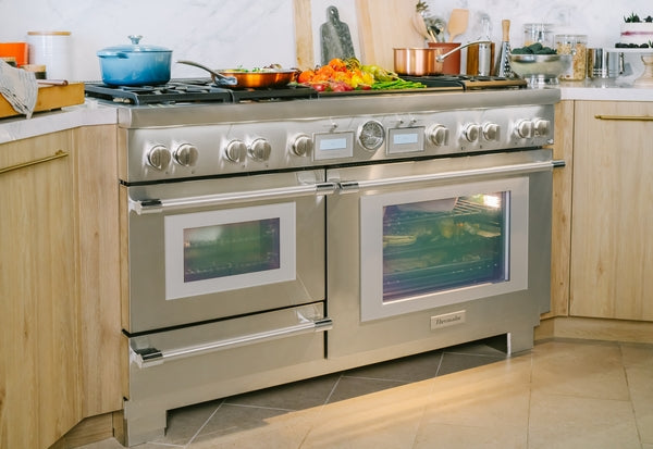 Stainless steel dual fuel professional range with double ovens and multiple control knobs in modern kitchen setting