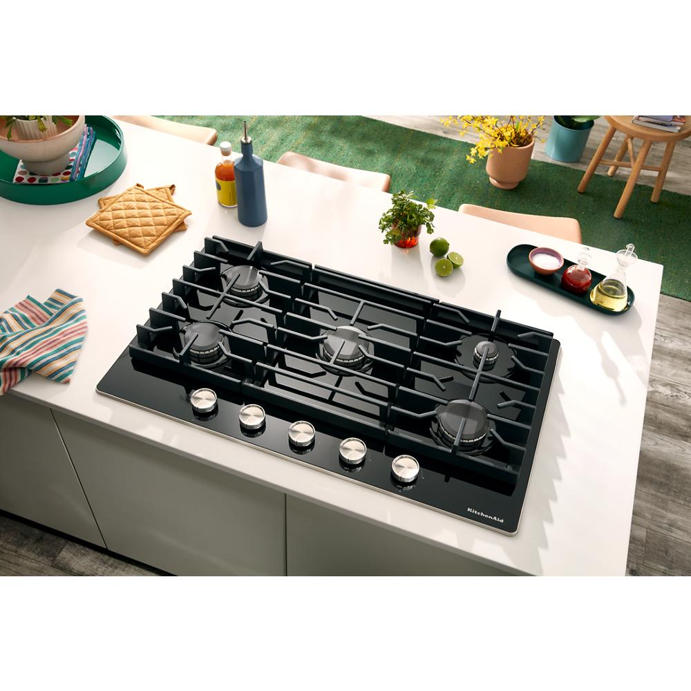Modern black gas-on-glass cooktop with five burners and silver control knobs in a bright kitchen setting for home improvement.