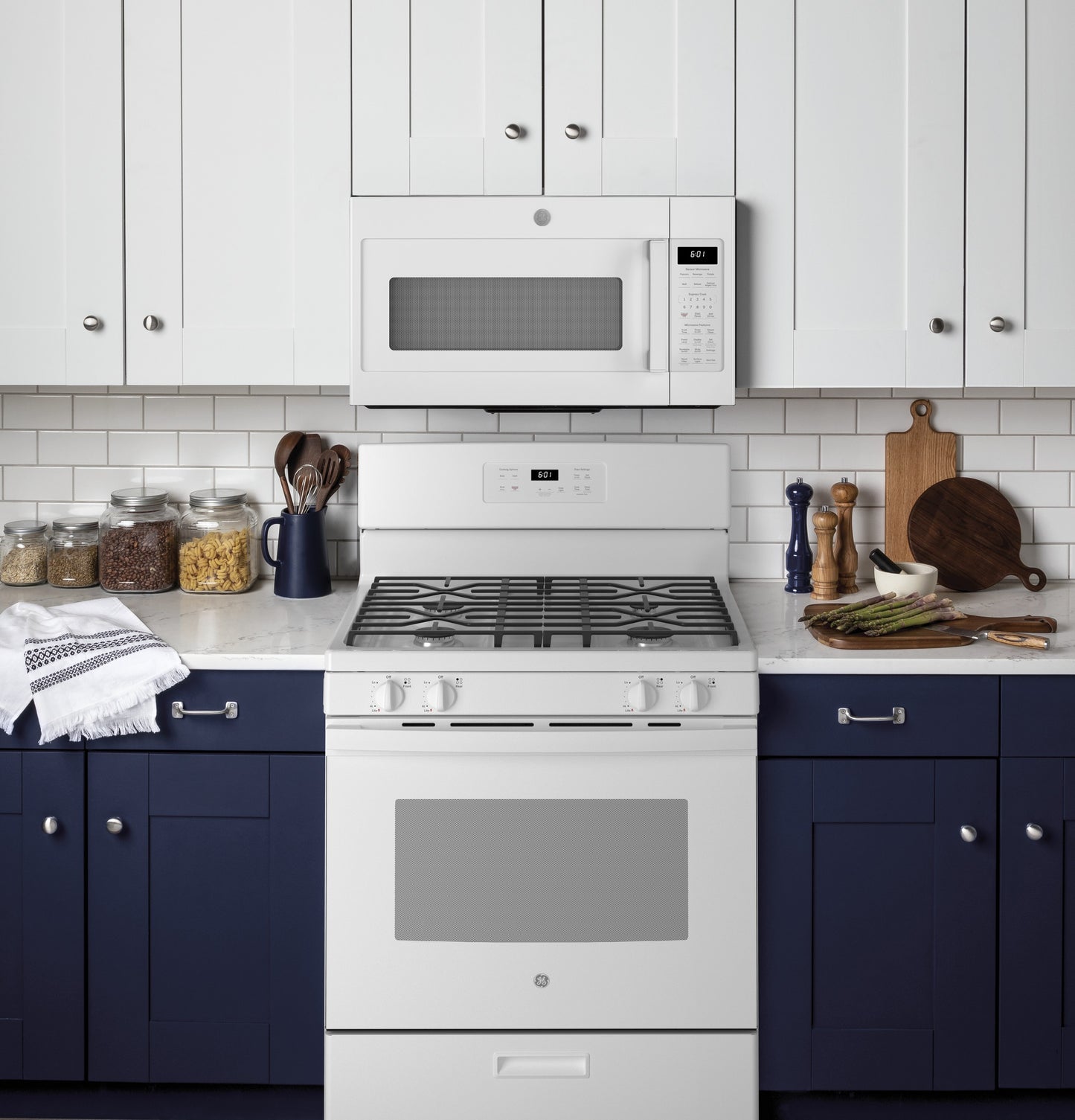 White freestanding gas range with five burners paired with white microwave in modern kitchen with navy cabinets