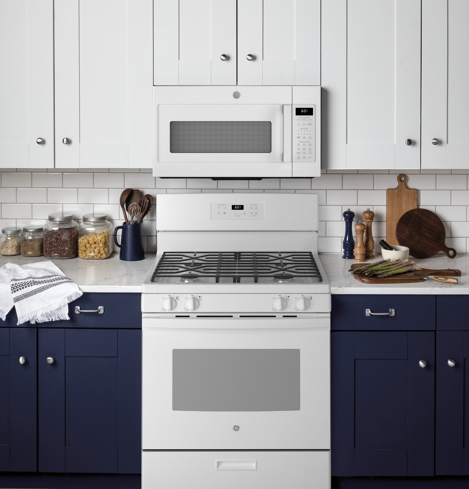 White freestanding gas range with five burners paired with white microwave in modern kitchen with navy cabinets