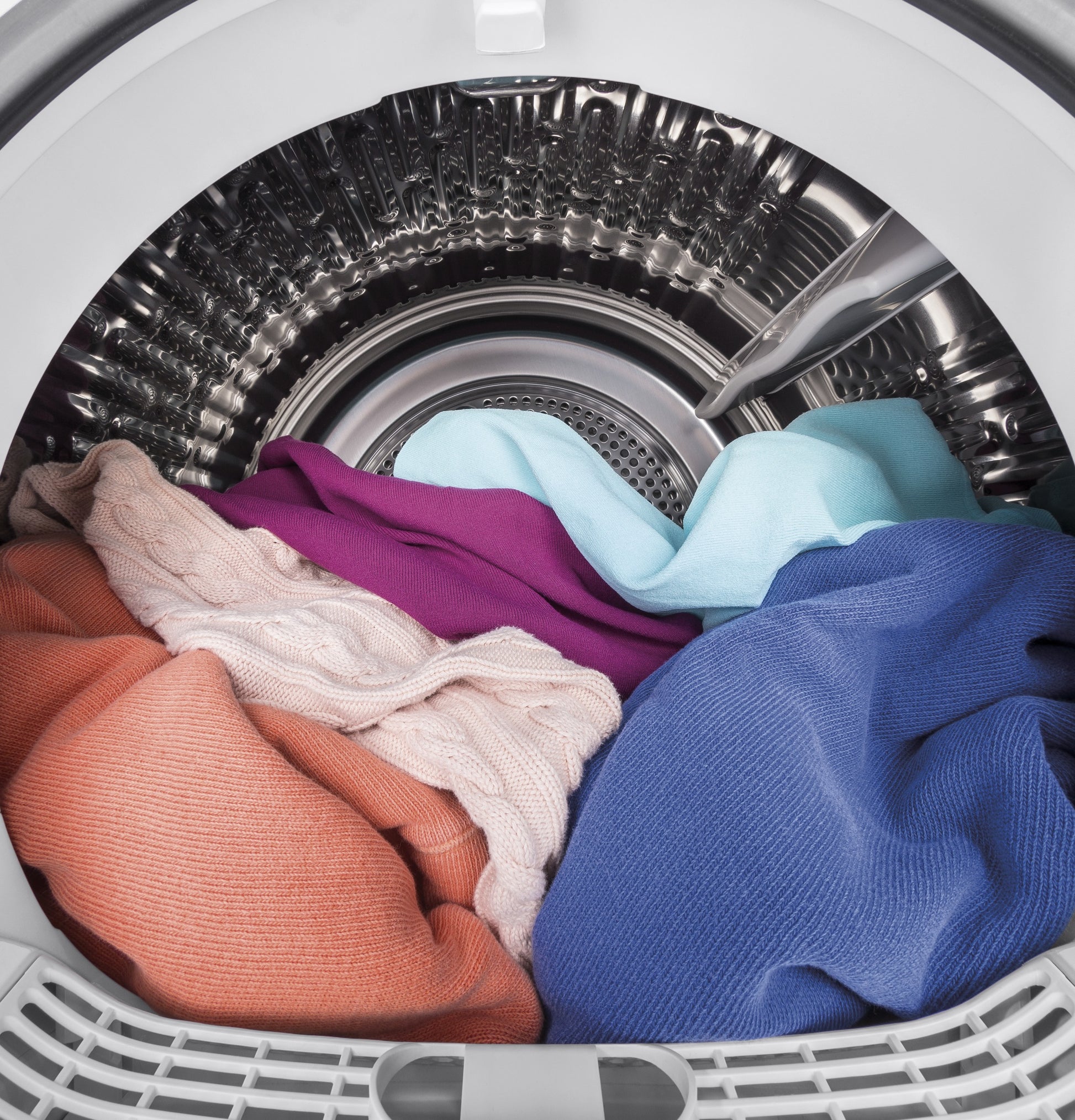Inside view of vented electric dryer drum with mixed colorful laundry in stainless steel basket from appliance collection