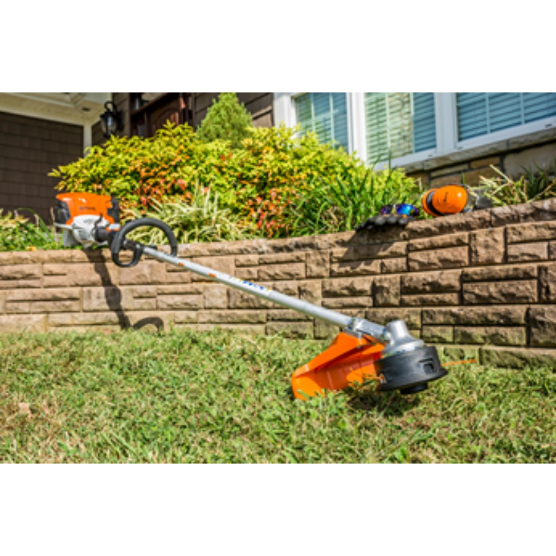 Orange and silver loop handle string trimmer resting on a lawn against a garden wall for landscaping tasks