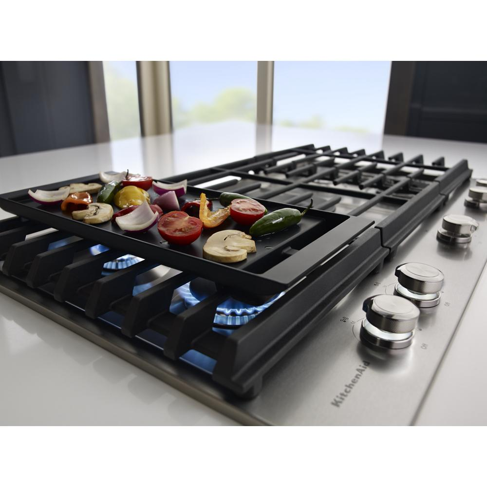 Black griddle with vegetables cooking on a stainless steel 36-inch gas cooktop with five burners from KitchenAid collections