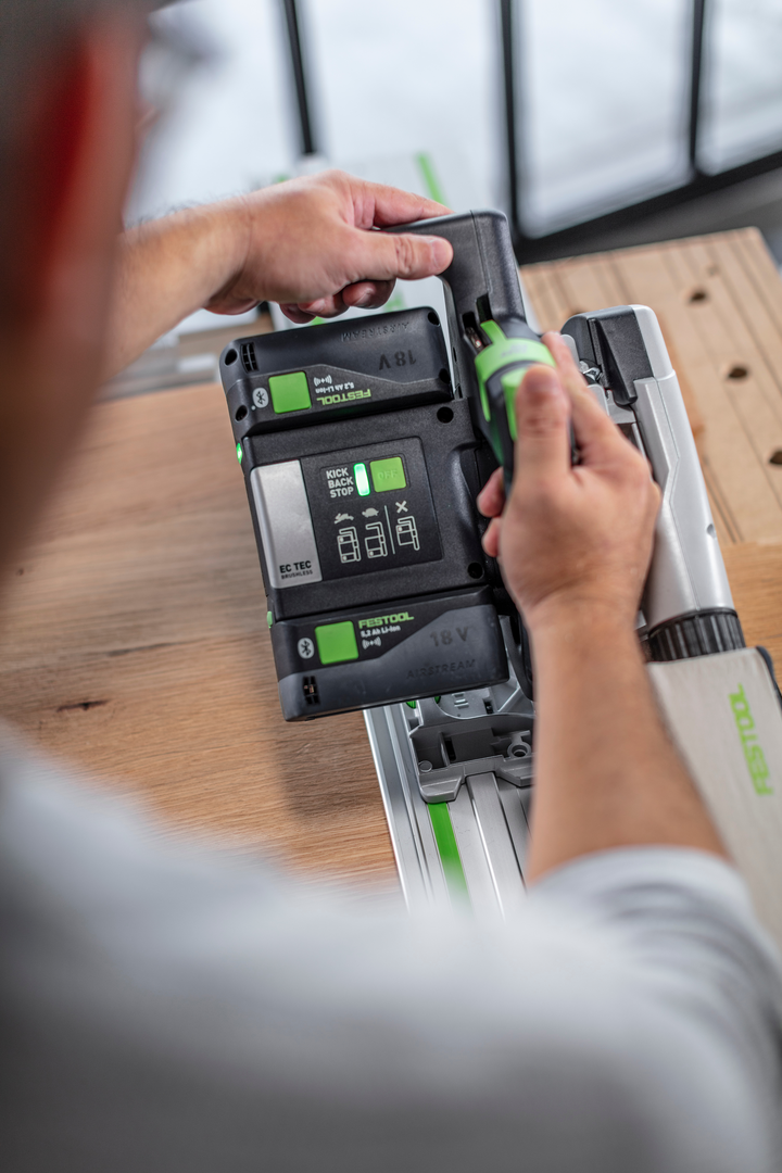 Person inserting 18V battery into cordless Festool track saw on wooden workbench in power tools workshop