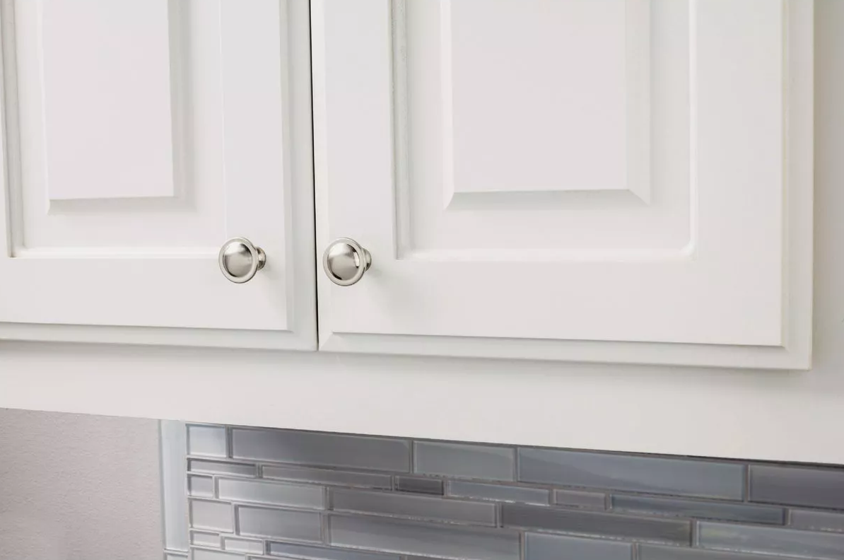 Satin nickel mushroom knobs installed on white cabinet doors above gray glass tile backsplash in home improvement setting