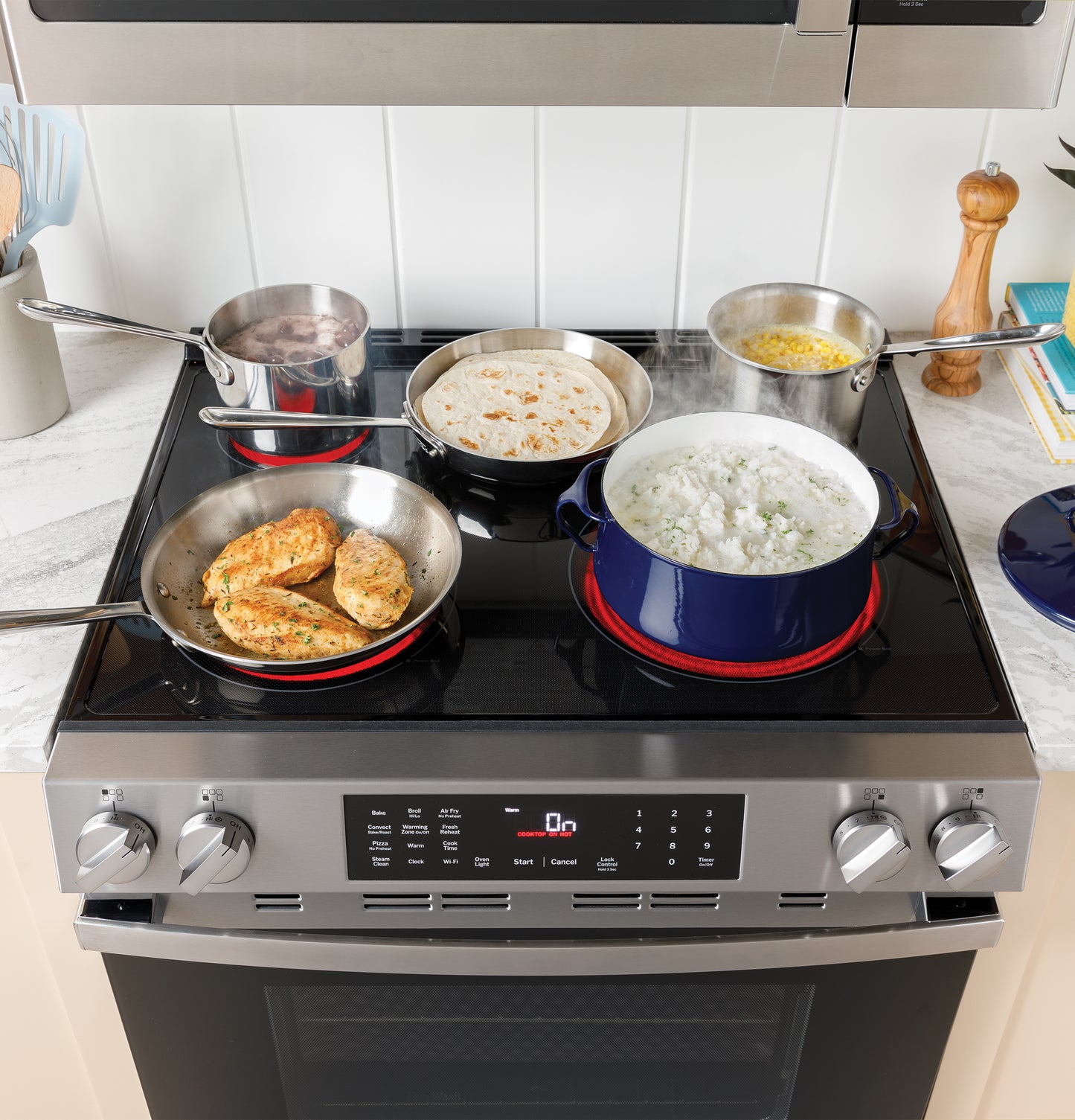 Stainless steel and blue pots with food cooking on a GE ENERGY STAR slide-in electric range in a modern kitchen setting