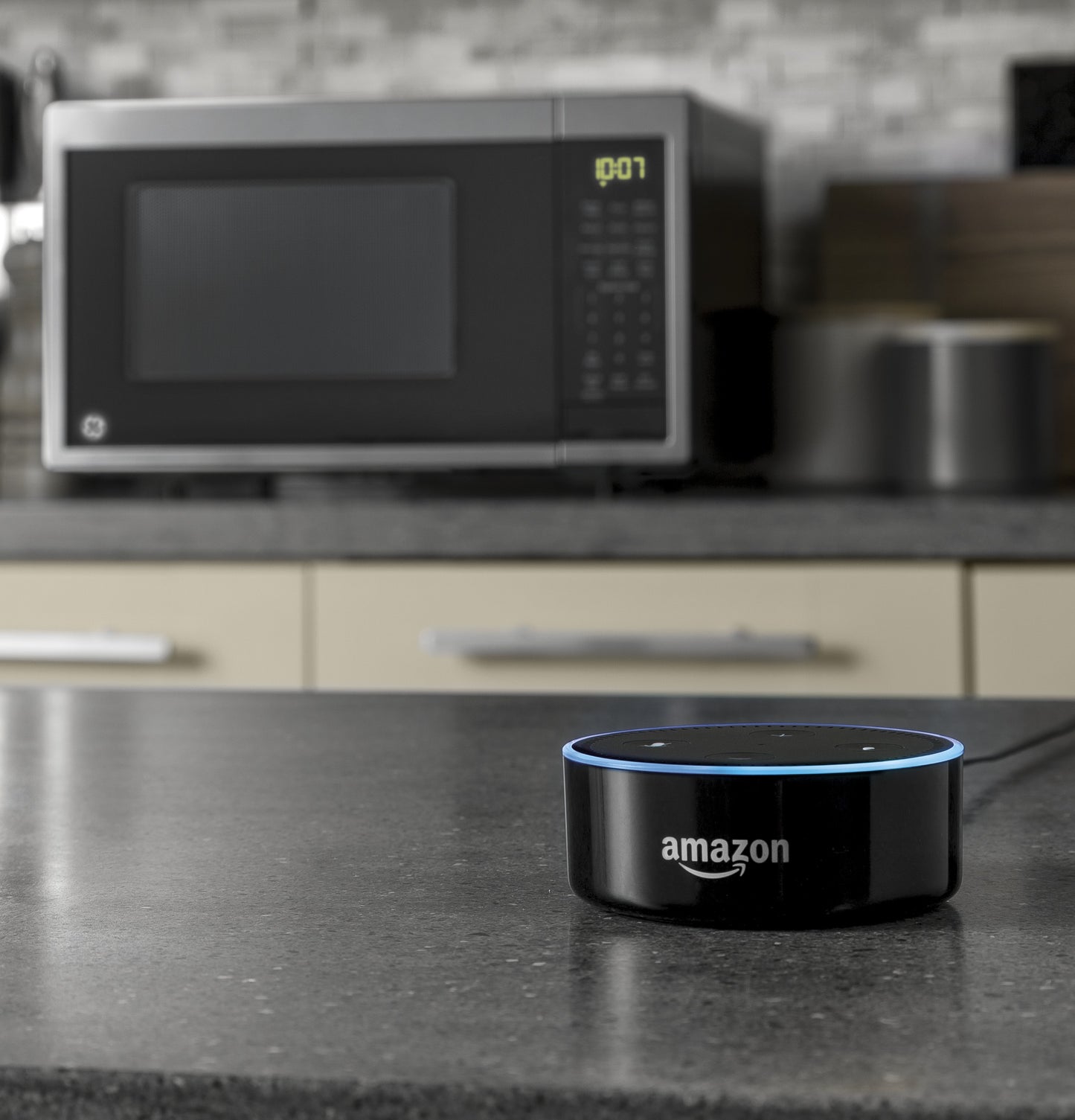 Black Amazon smart speaker with blue ring light on kitchen counter near modern countertop microwave oven