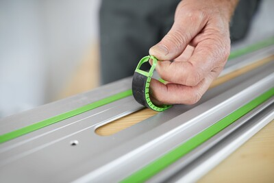 Hand securing green adhesive pad onto aluminum guide rail for woodworking tool accessories and home improvement.