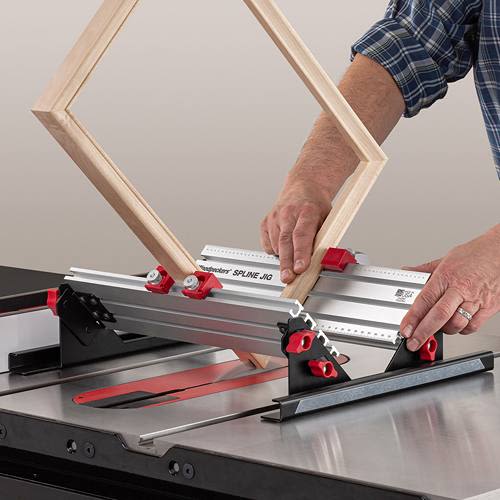 Woodworking spline jig with red adjustment knobs securing wood frame on table saw for accurate joinery cuts