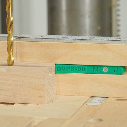 Green plastic stop block fitted into wooden jig with drill bit and metal ruler for precise woodworking cuts