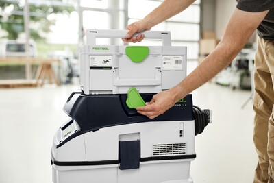 Person attaching a compact HEPA dust extractor to modular Festool dust collection unit in workshop setting