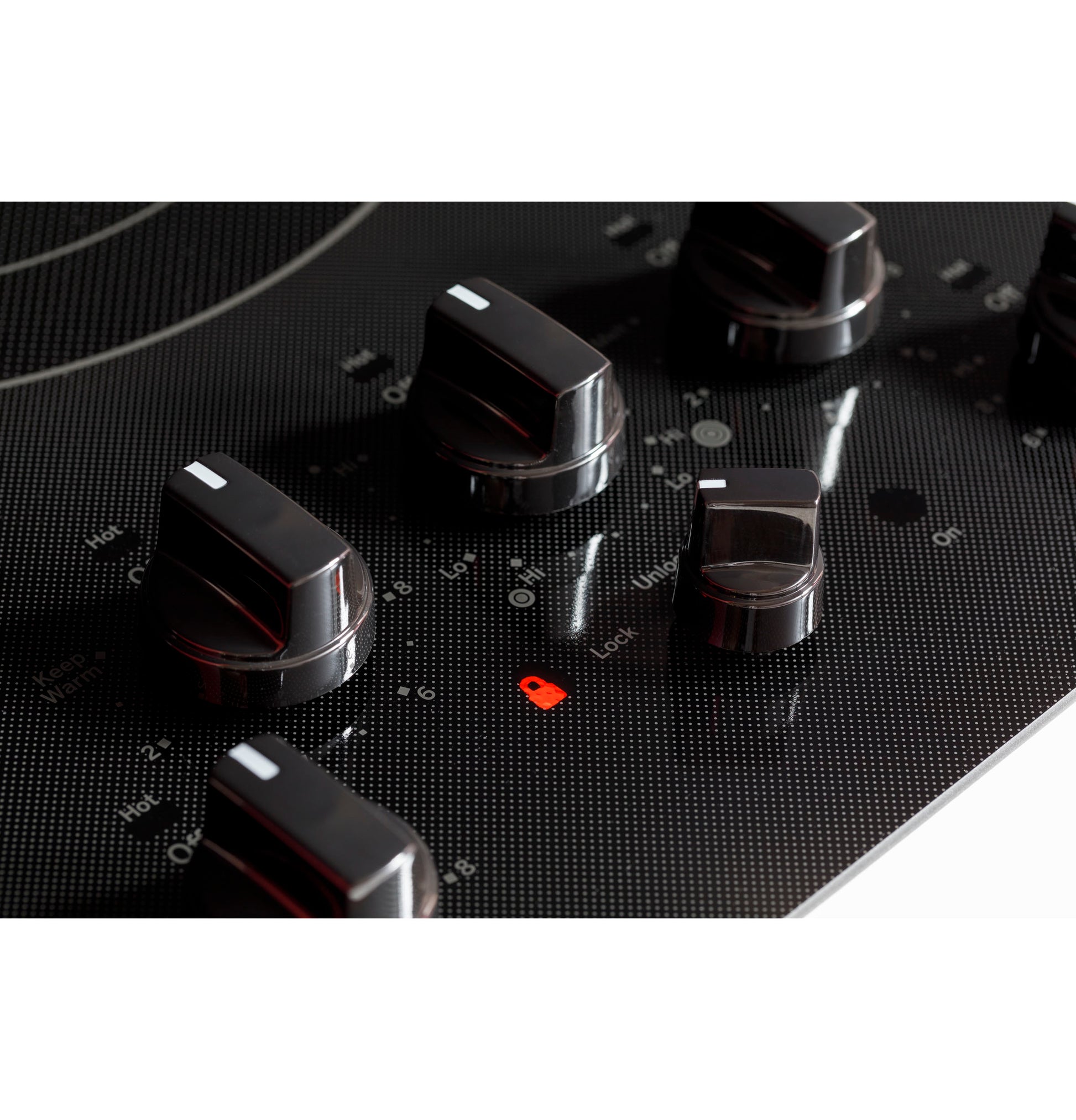 Close-up of black electric cooktop with knob controls and red lock indicator light in kitchen appliance setting