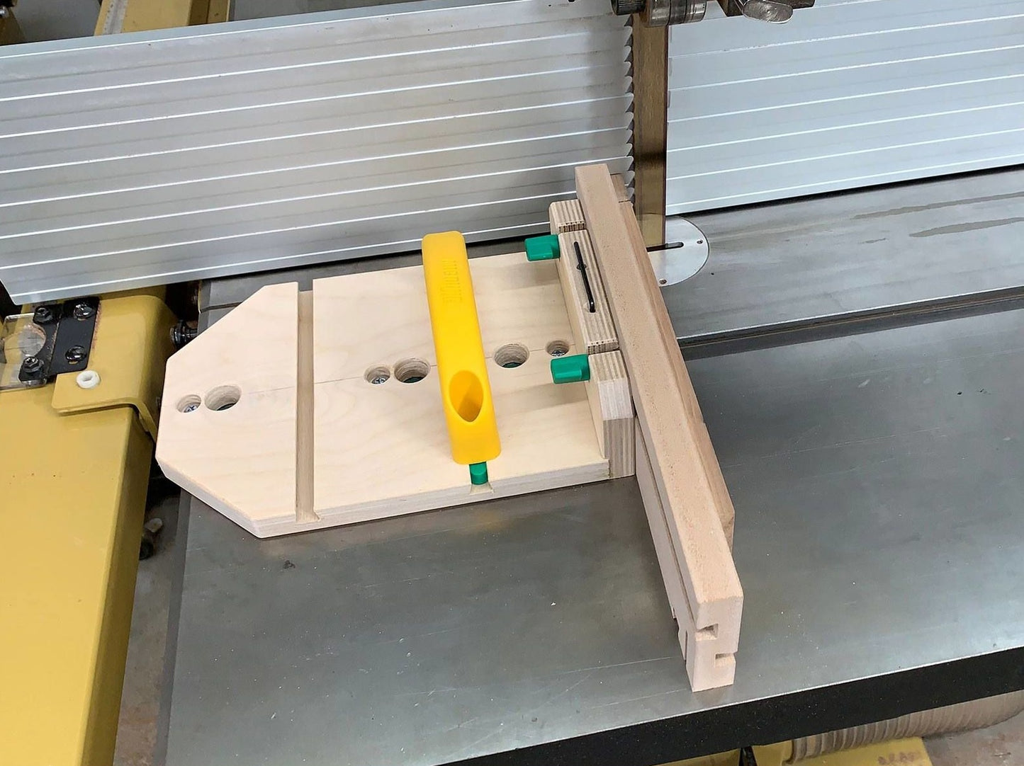 Light wood jig with yellow handle and green clips secured on table saw for precision cutting in home improvement tasks