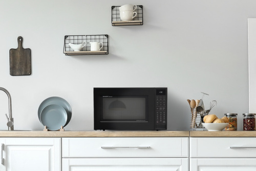 Black convection microwave oven on wooden countertop in modern kitchen with white cabinets and wall shelves