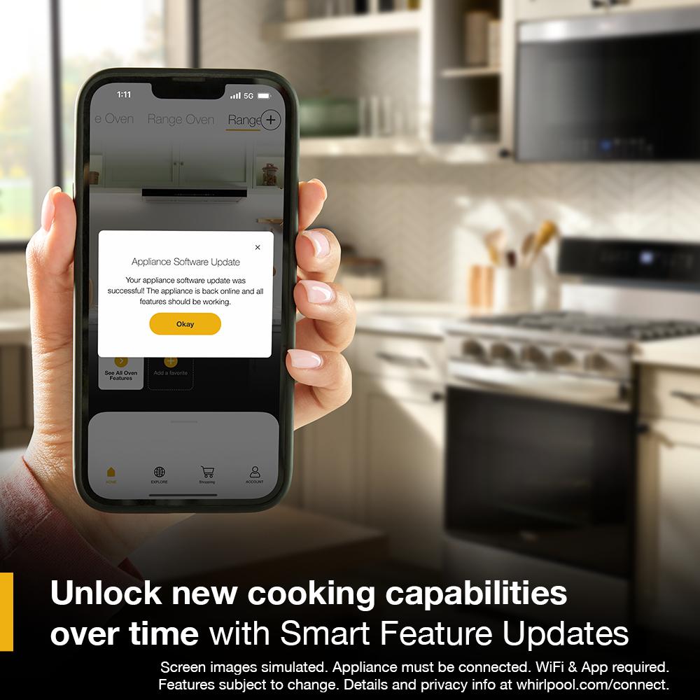 Hand holding smartphone showing successful appliance software update with gas range and microwave in modern kitchen background