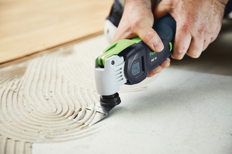 Person using a Festool oscillating tool with a scraper blade removing tile adhesive in a woodworking or home improvement setting