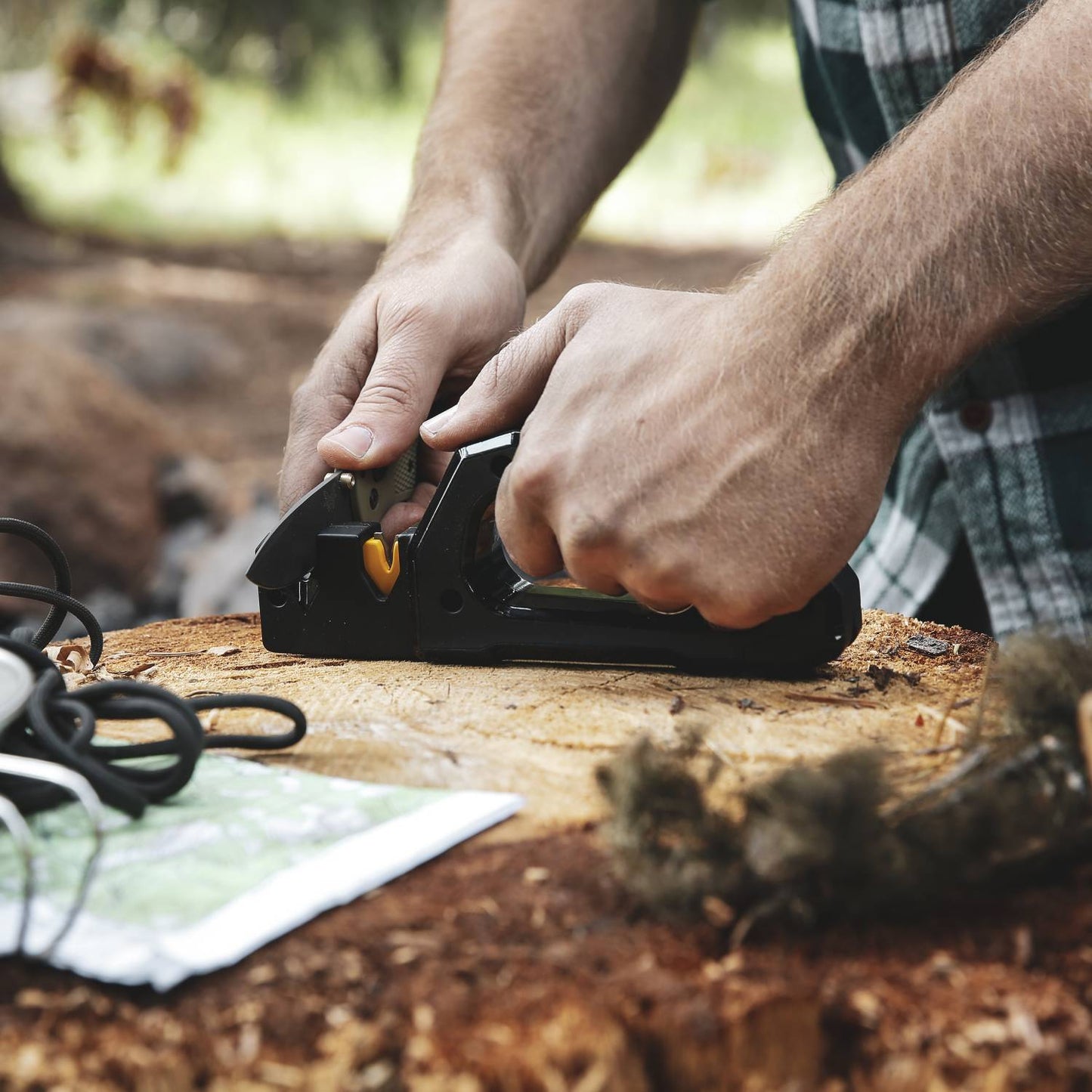 Hands using black and yellow sharpener on wood surface outdoors with map nearby for home improvement tools