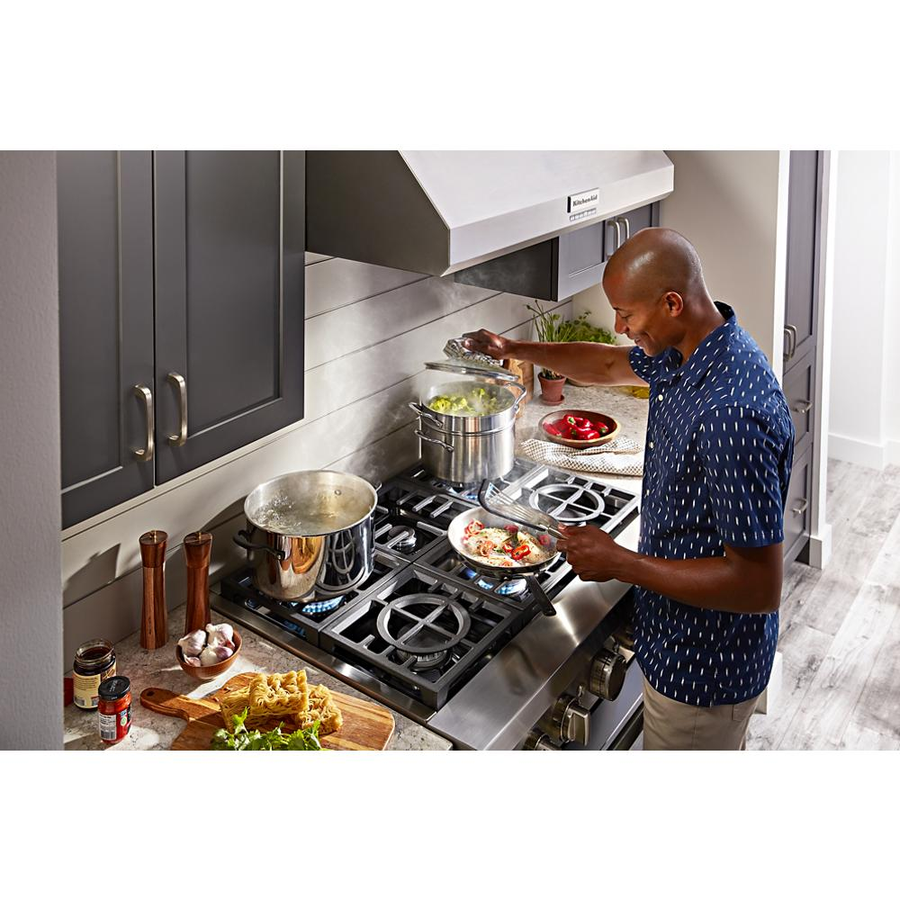 Man cooking pasta and vegetables on gas stove beneath stainless steel wall-mount canopy range hood in kitchen