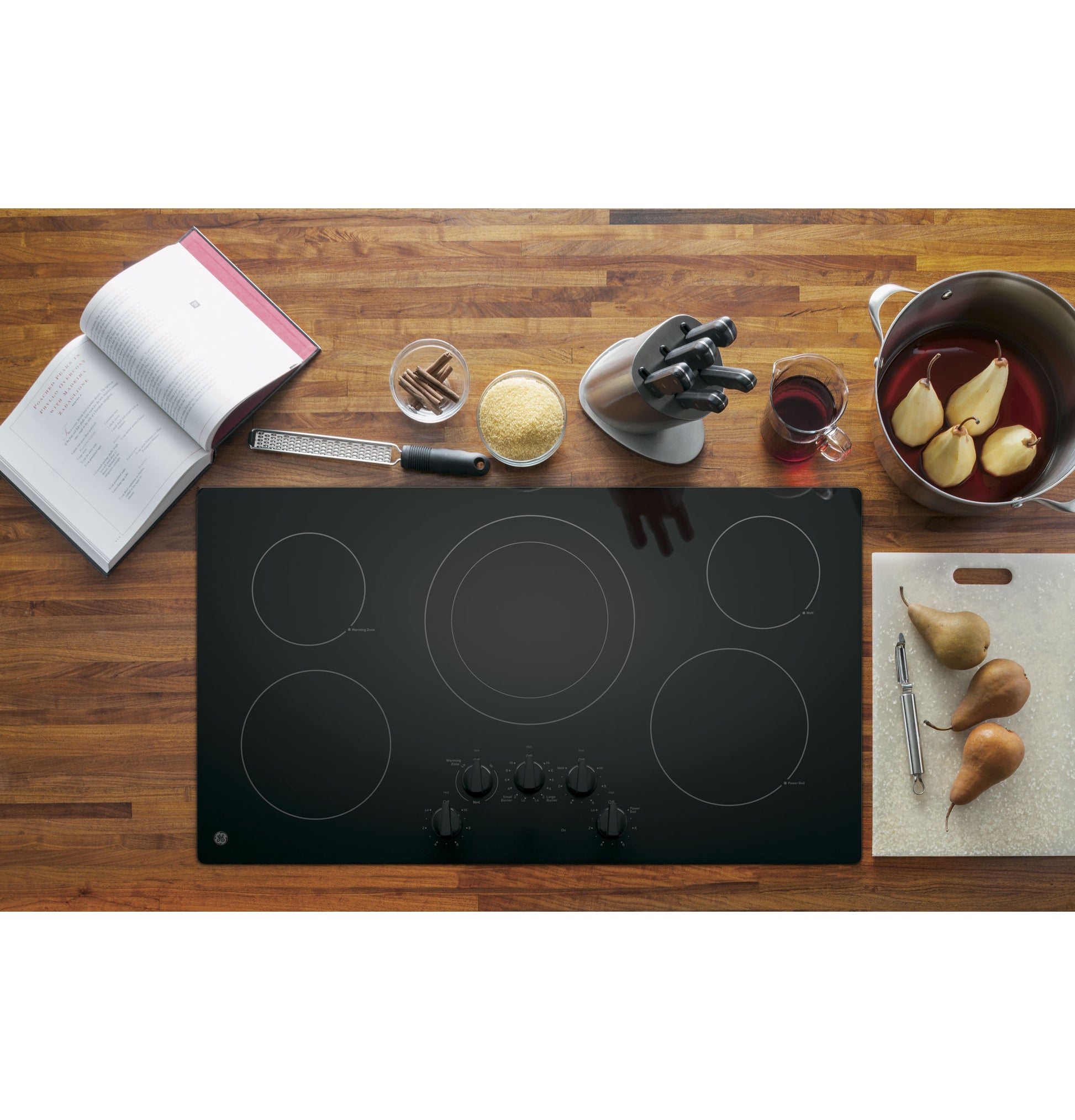 Black electric cooktop with five burners and front knob controls on wooden countertop in kitchen appliances setting