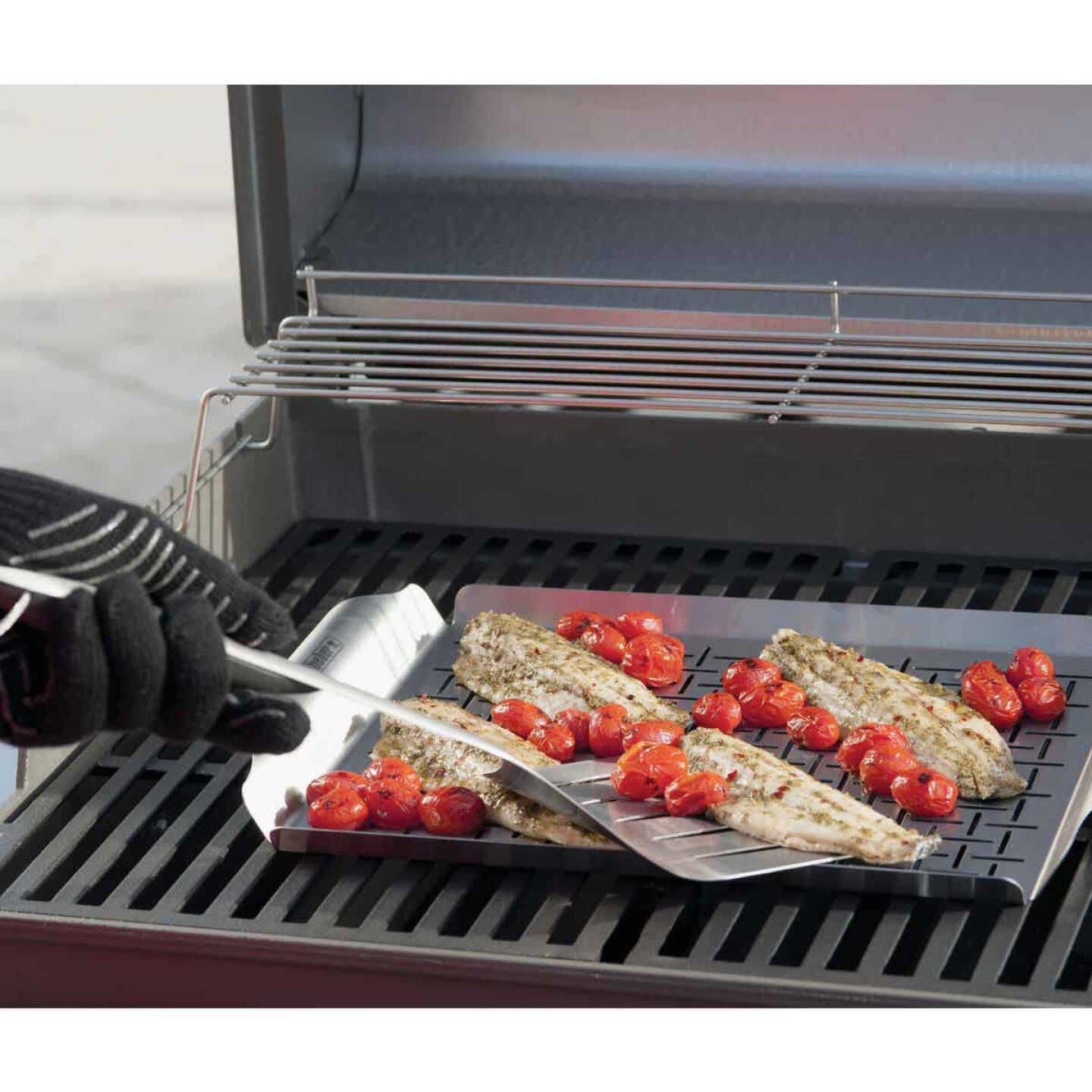 Rectangular stainless steel grilling pan with slotted surface holding grilled fish and cherry tomatoes on gas grill