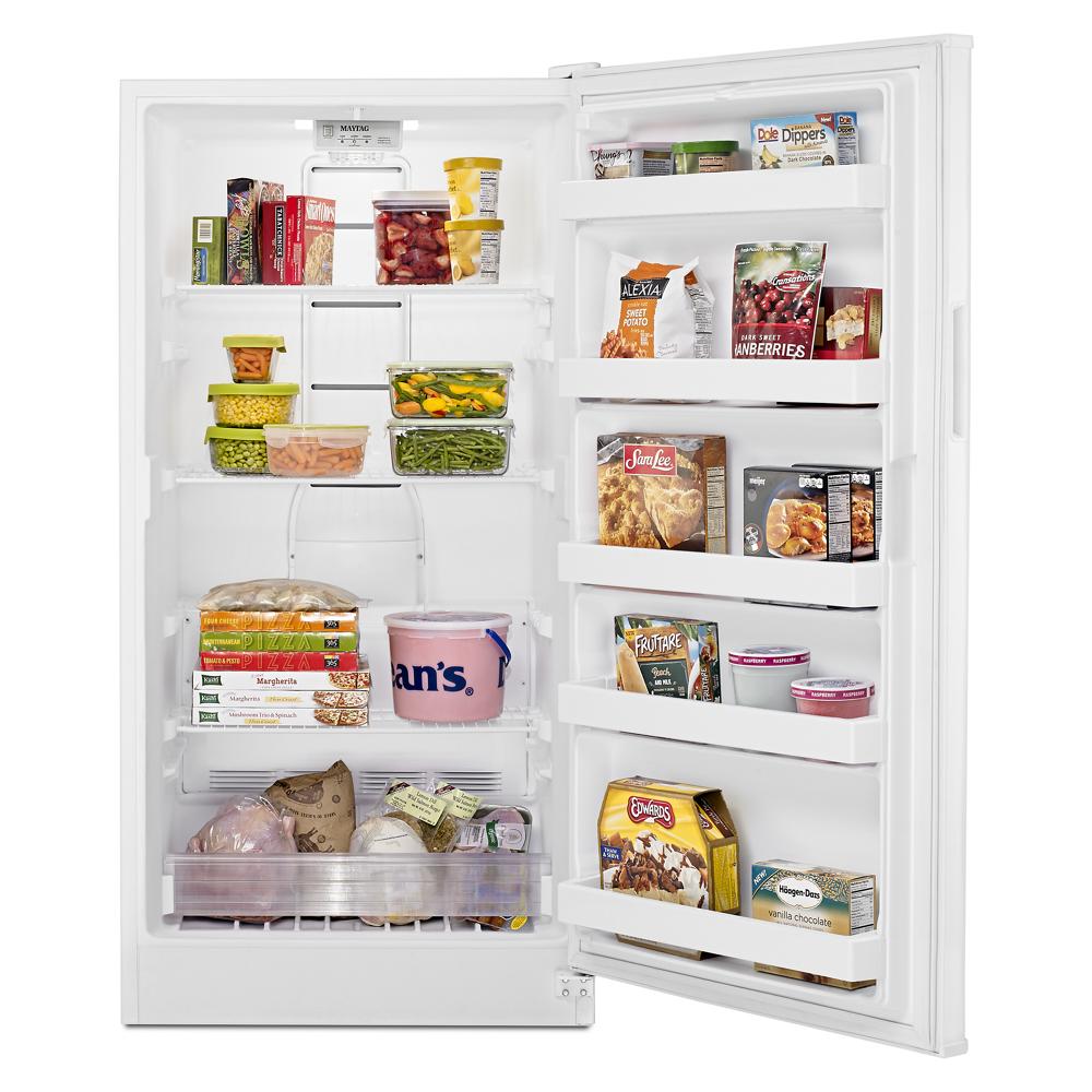 Open white upright freezer filled with food containers and packaged frozen goods for kitchen and appliances collections
