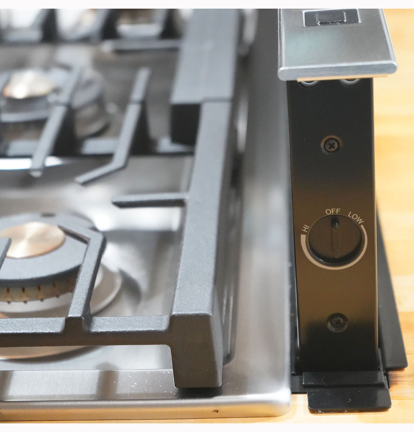 Close-up of black control knob on stainless steel telescopic downdraft vent beside gas range in kitchen appliances collection