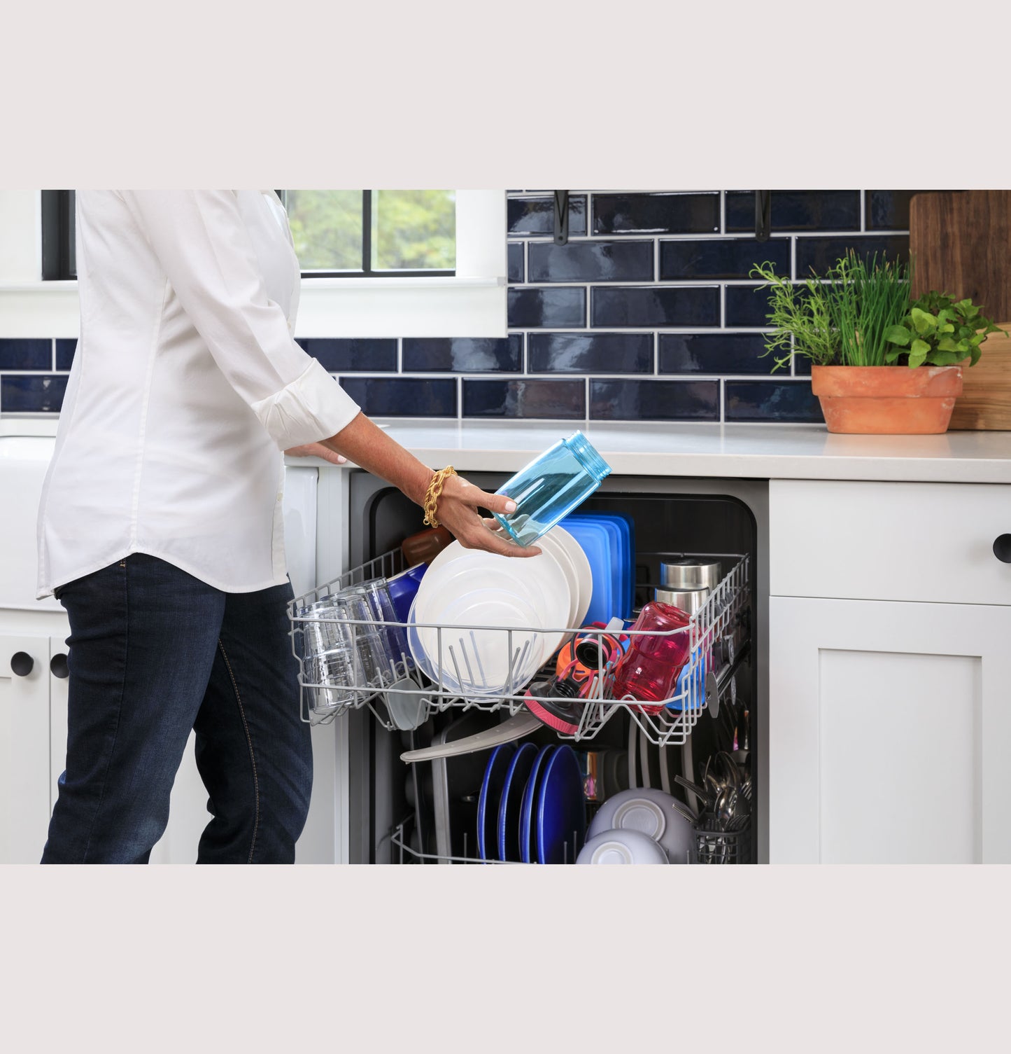 Person loading clean dishes into a built-in dishwasher with front controls in a kitchen with blue tile backsplash