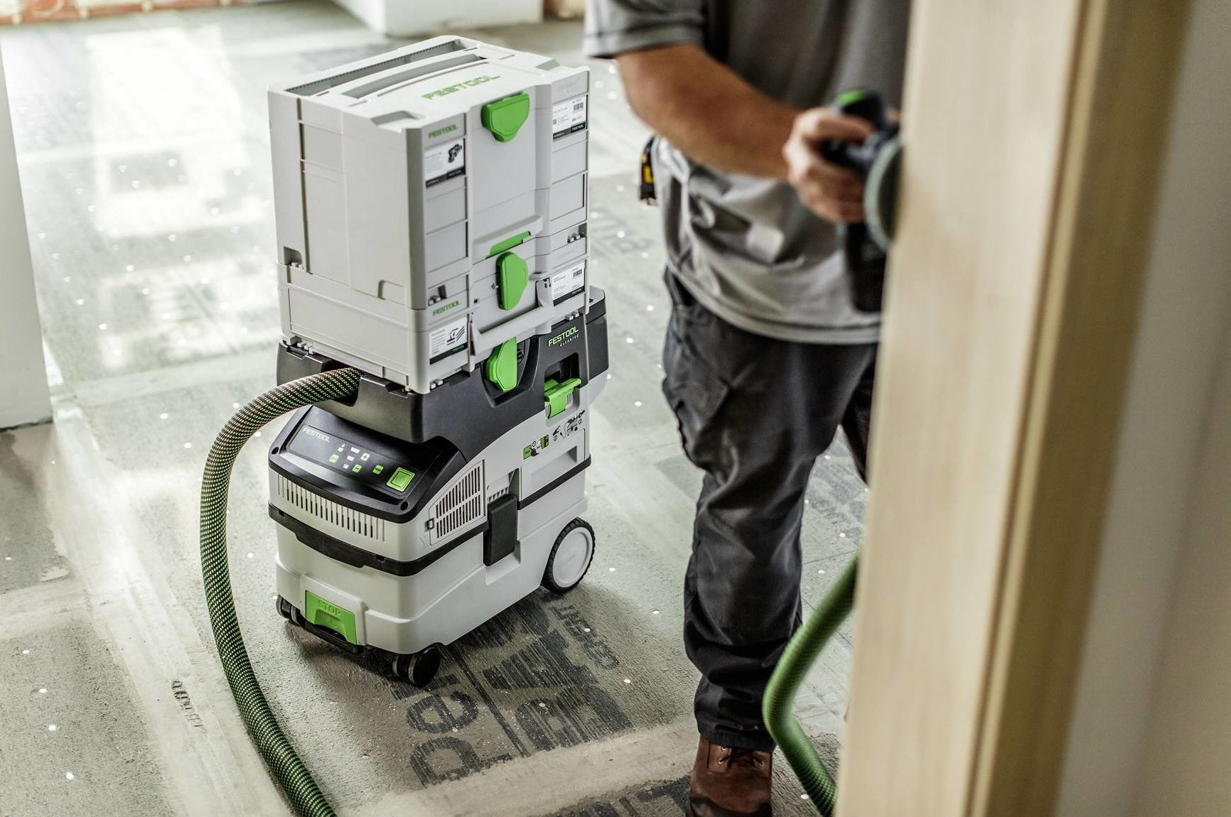 Cordless HEPA dust extractor with connected storage boxes, used by worker sanding wood in home improvement project